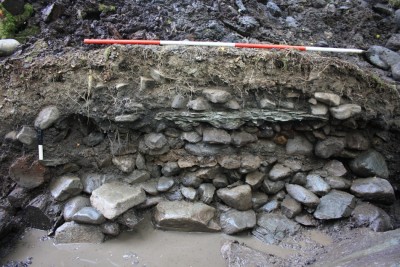 Figure 4. The hearth complex in section; the massive foundation slabs are visible at the base of the section, above which are the mounds of cobbles between hearthstones; at the base of the section to the left are the alder foundation timbers. 